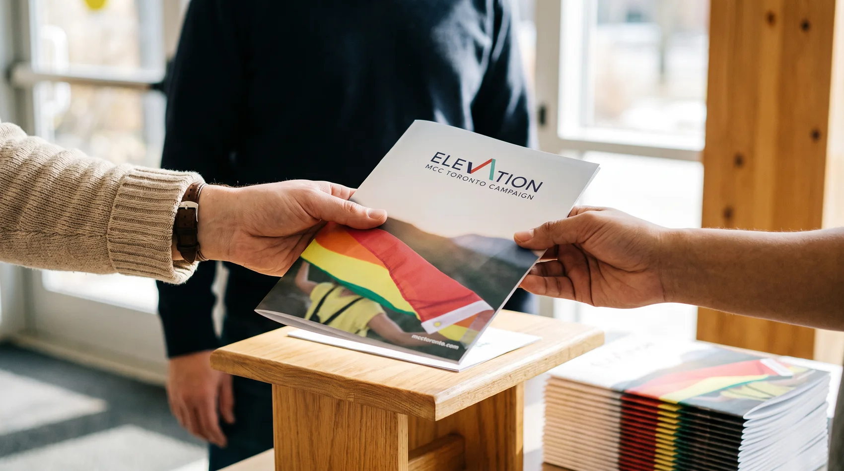 A copy of the Elevation case for support being handed from one person to another, with a stack of them on a table